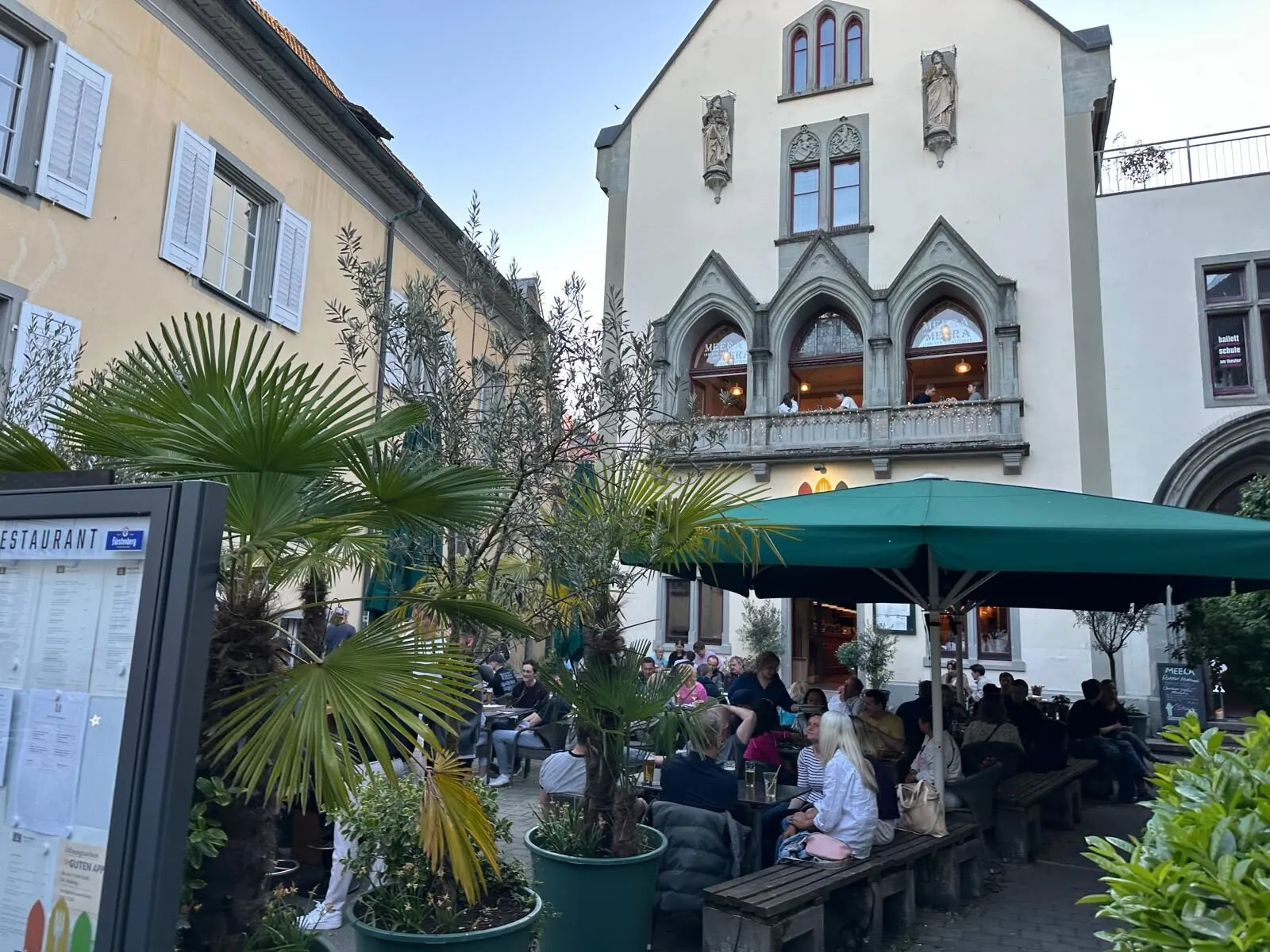 Belebte Aussenterrasse im Innenhof von The Dom Konstanz mit Palmen und Sonnenschirmen