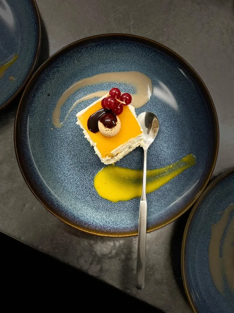 Dessert-Kuchenstück mit Beeren und Sauce auf blauem Teller – The Dom Konstanz