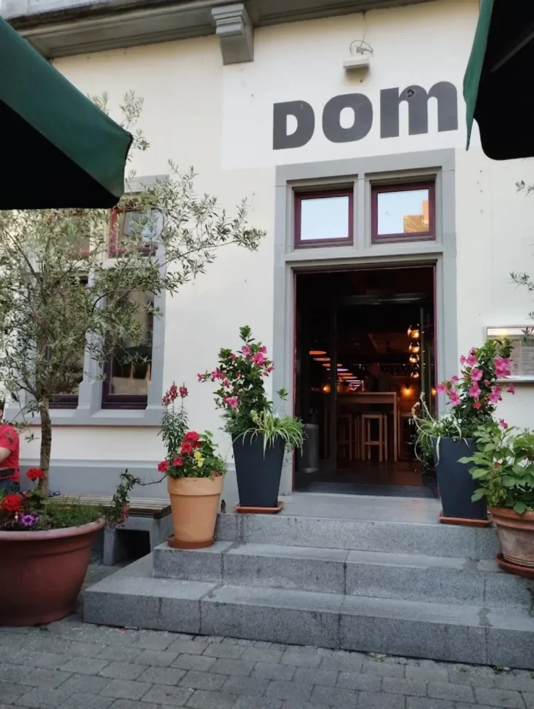 Eingang The Dom mit Blumen und Olivenbaum