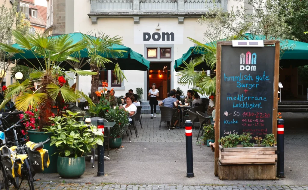 The Dom Sommertterrasse mit Palmen und Gästen