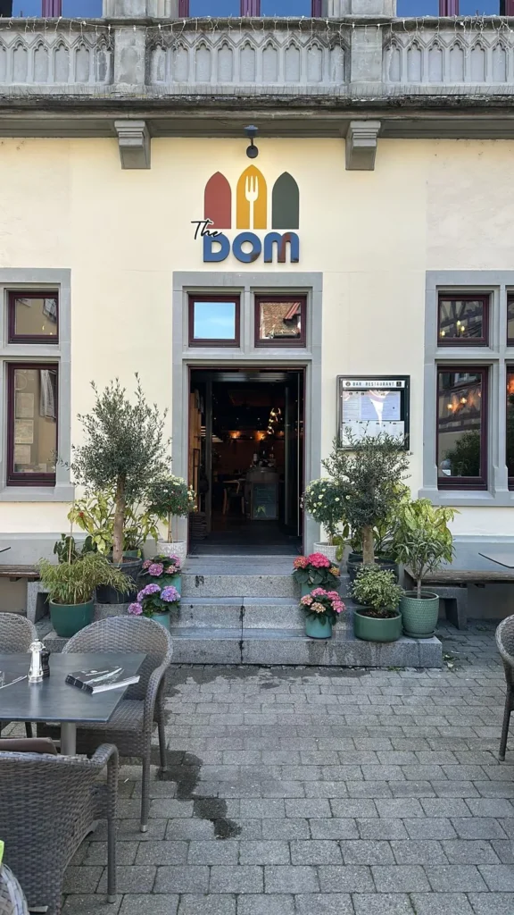 Abendlicher Eingangsbereich des The Dom Restaurant mit warm beleuchtetem Interieur durch die offene Tür