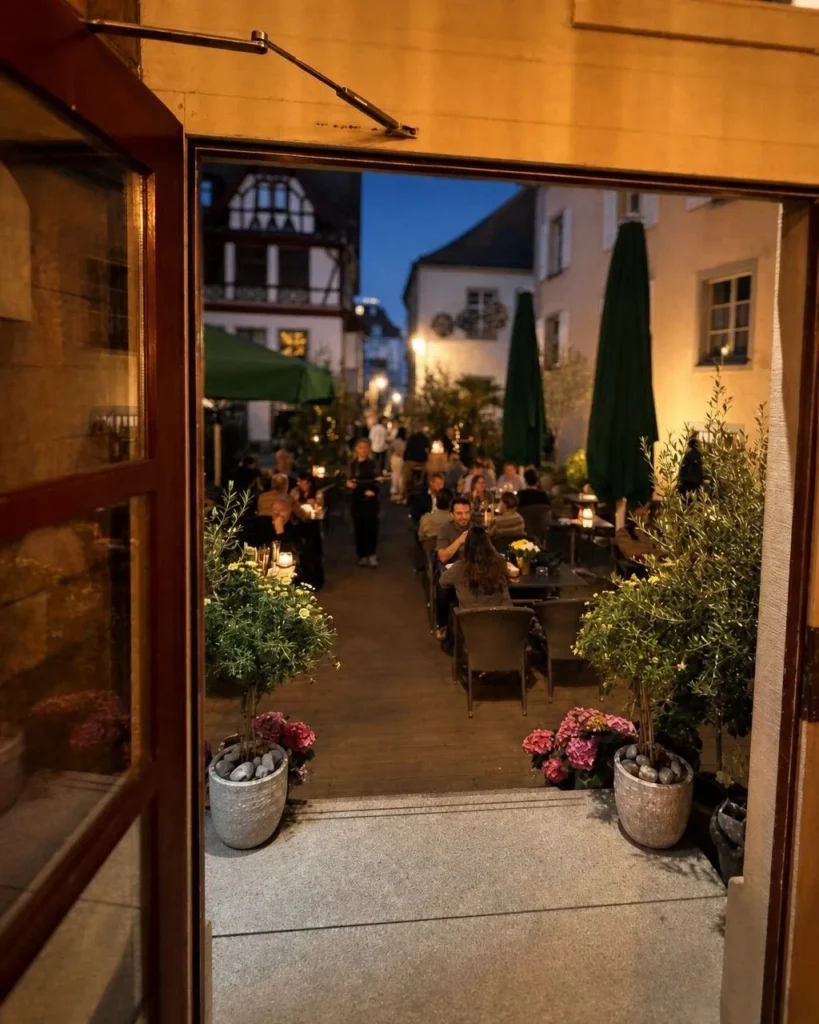 Blick durch die geoeffnete Tuer auf die abendliche Terrasse von The Dom Konstanz mit Gaesten