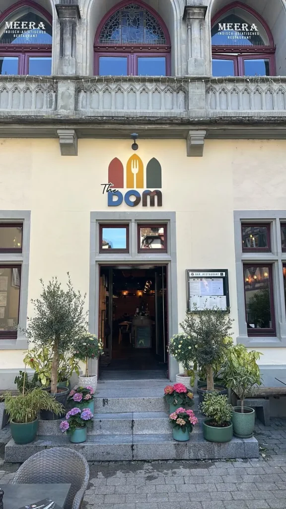 Eingang des Restaurants The Dom Konstanz mit Logo, Olivenbaeumen und Blumen in der Altstadt