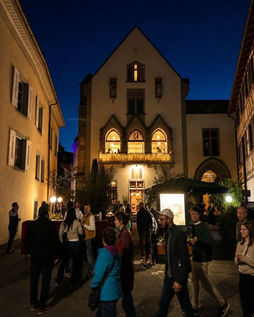 Beleuchtete gotische Fassade von The Dom Konstanz am Abend mit Gaesten in der Altstadt