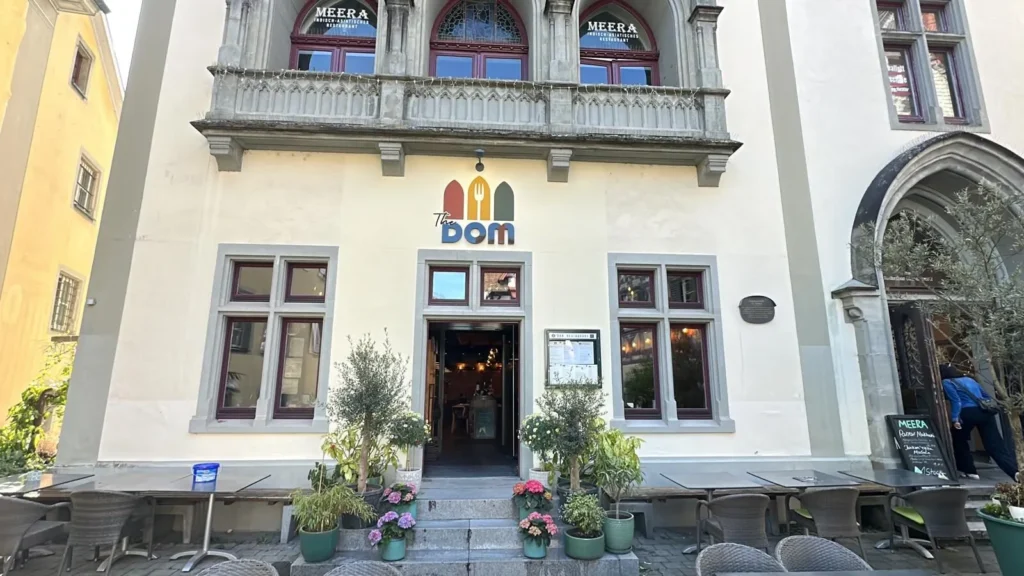 Historische Fassade des Restaurants The Dom Konstanz mit Aussenplaetzen, Blumen und gotischem Balkon