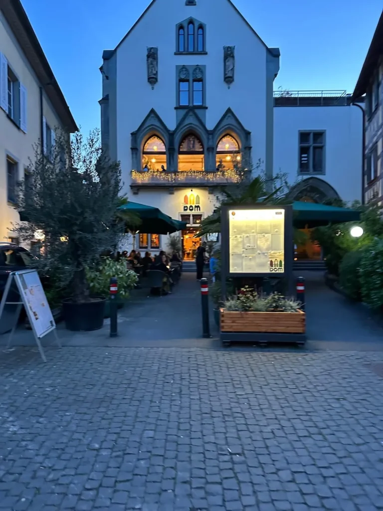 Gotische Fassade von The Dom Konstanz in der Daemmerung mit beleuchteter Speisekarte und Terrasse