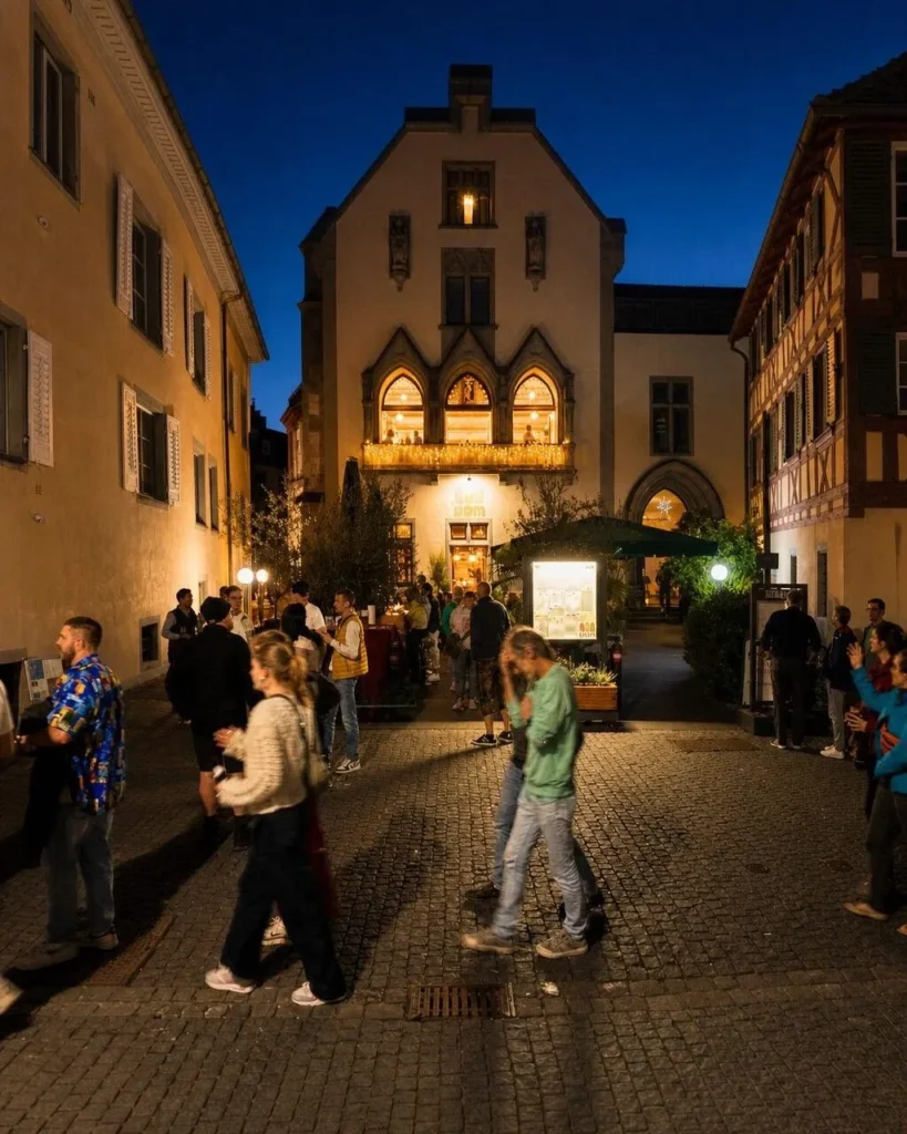 Blick aus der Konstanzer Altstadt-Gasse auf The Dom bei Nacht mit Passanten und Lichterketten