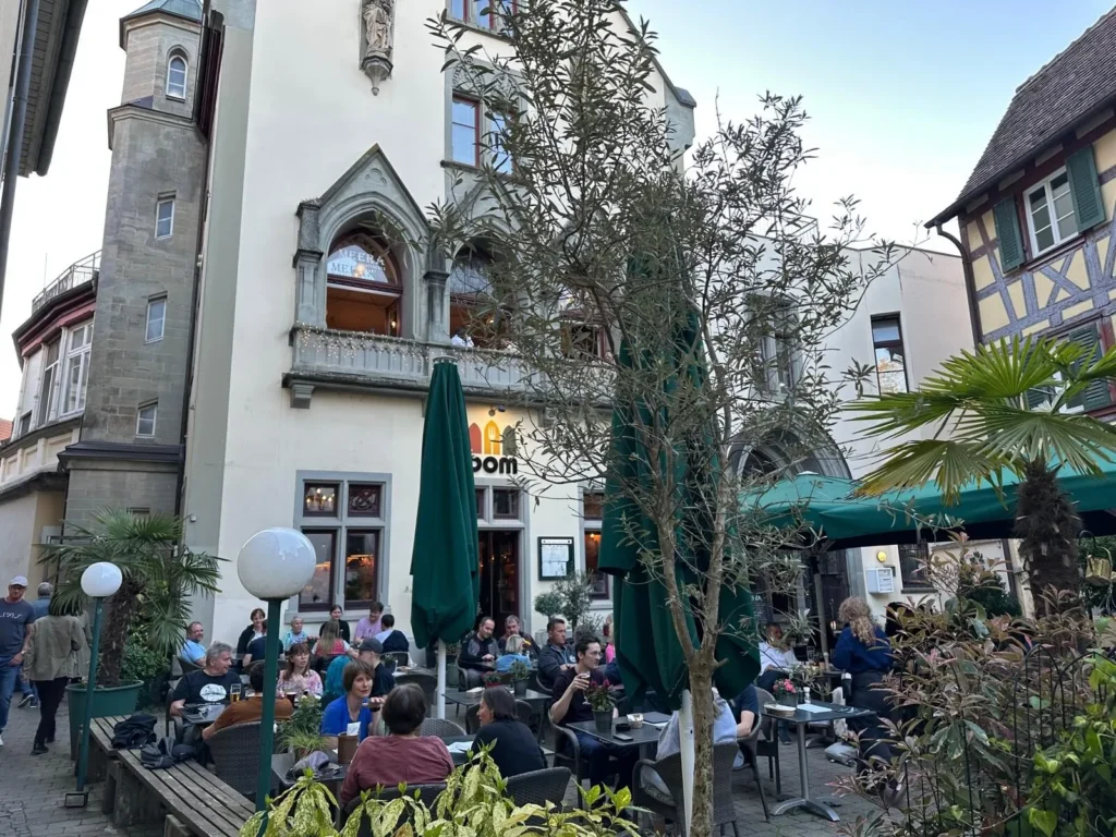 Historische gotische Fassade von The Dom Konstanz mit voller Terrasse, Palmen und Fachwerk im Abendlicht