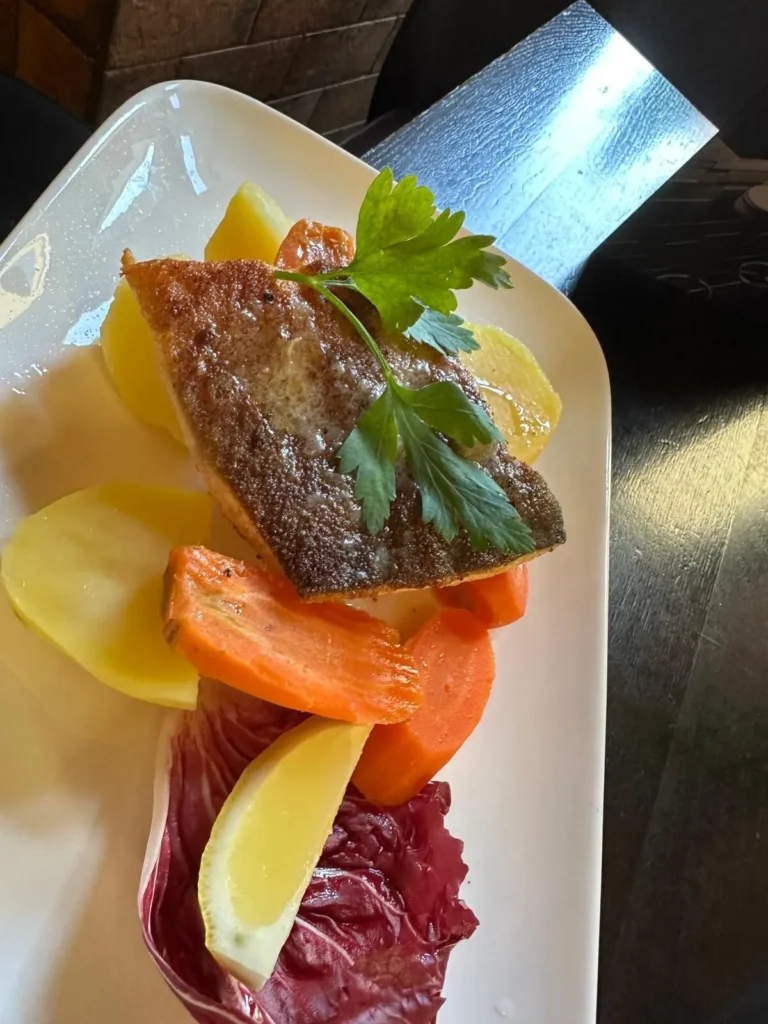 Gebratenes Fischfilet mit Petersilie, Karotten und Kartoffeln auf weissem Teller im The Dom