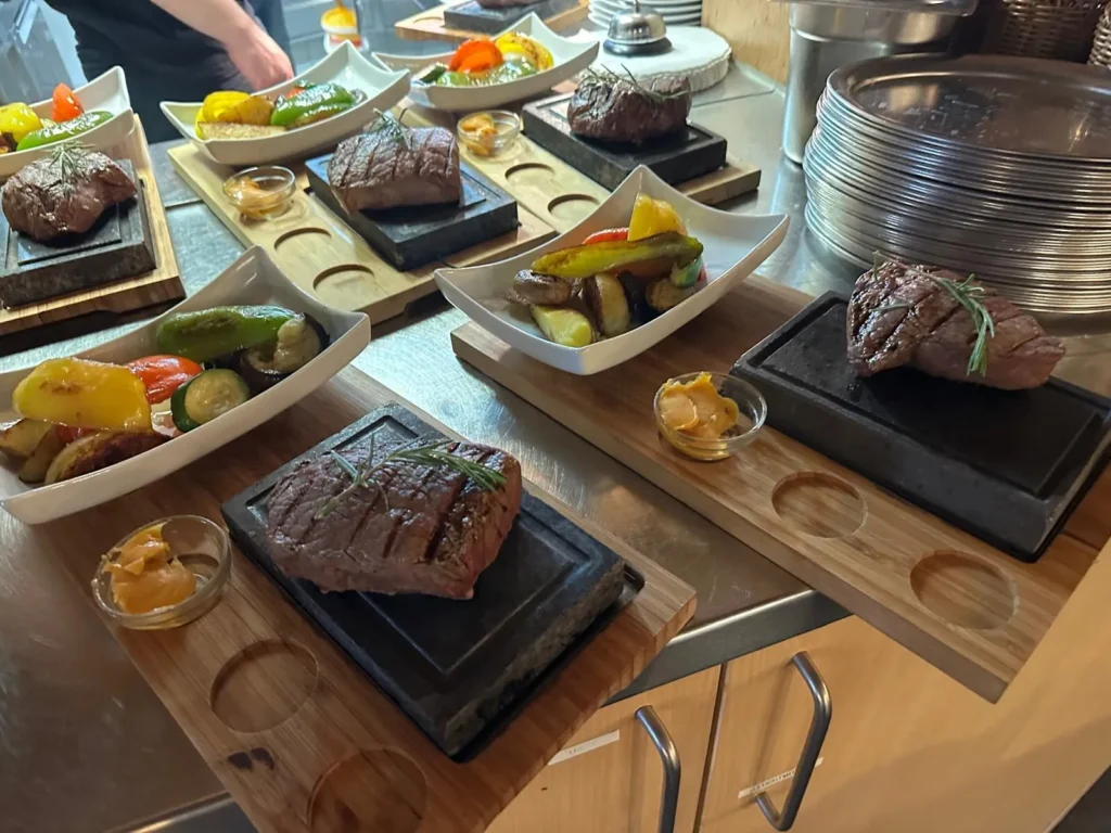Mehrere Steaks auf Lavastein mit Grillgemuese werden in der Kueche von The Dom angerichtet