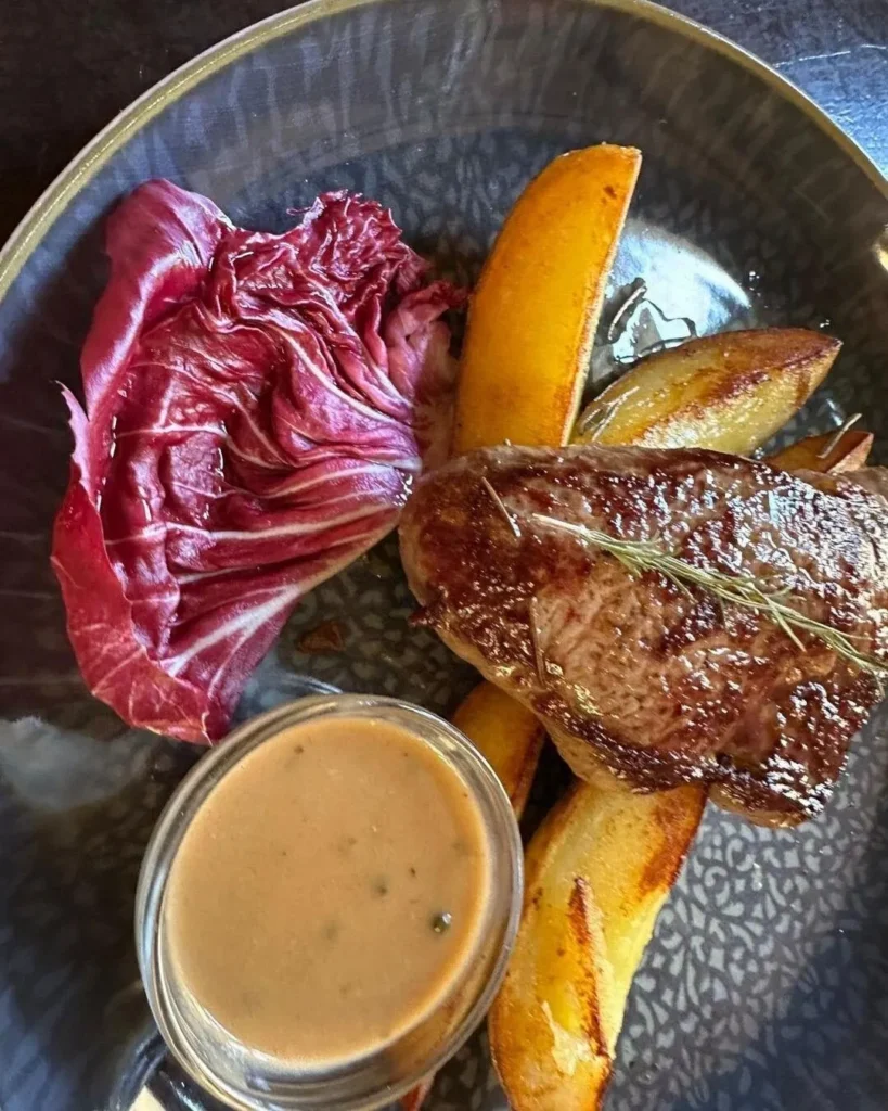 Saftig gegrilltes Steak mit Radicchio, Kartoffelecken und Pfeffersauce von oben im The Dom