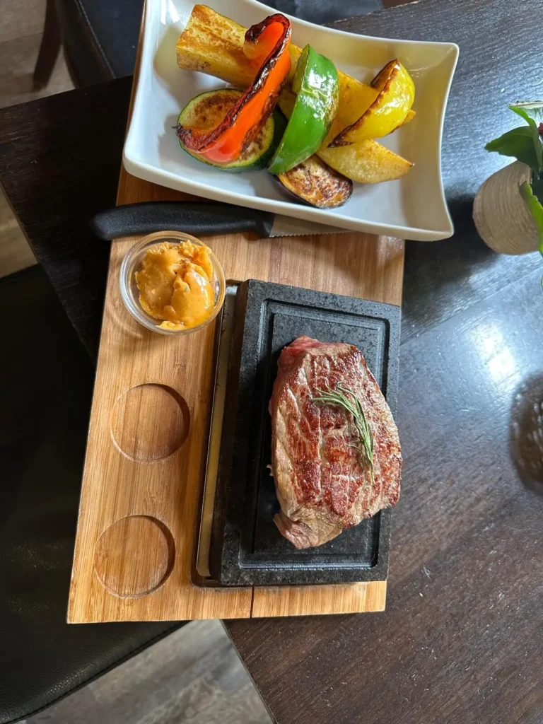 Gegrilltes Steak auf Steinplatte mit buntem Grillgemuese und Kraeuterbutter von oben bei The Dom Konstanz