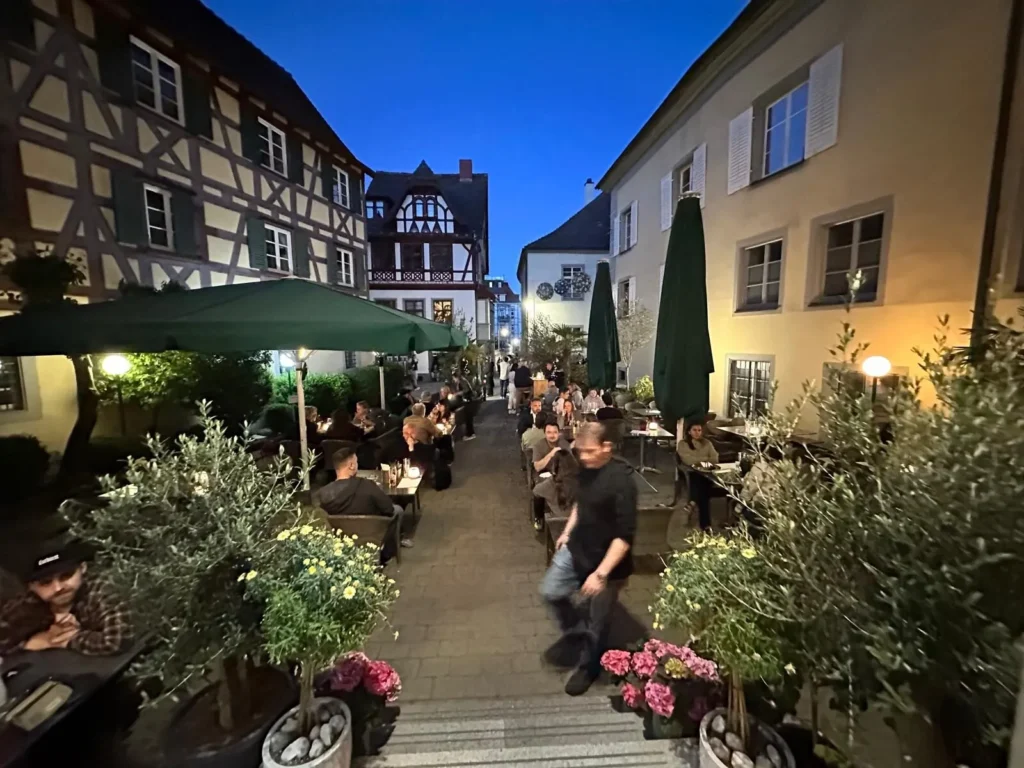 Abendstimmung auf der Terrasse von The Dom Konstanz mit Fachwerkhaeusern und Gaesten zur blauen Stunde