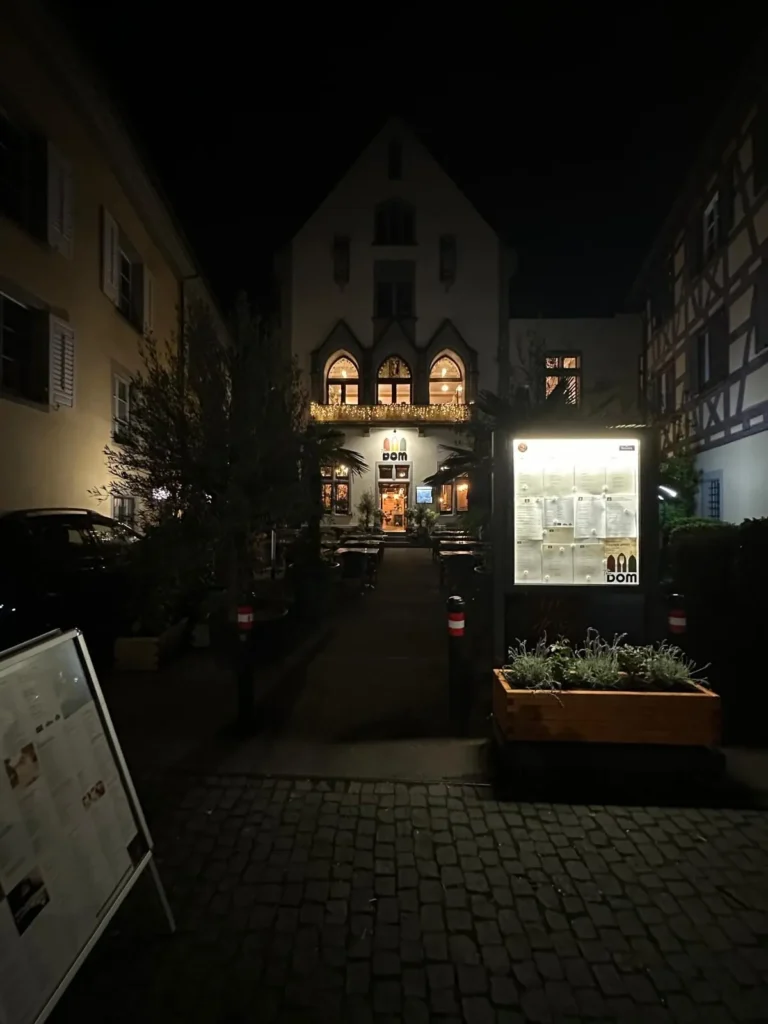 Blick aus der Konstanzer Altstadt-Gasse auf The Dom bei Nacht mit beleuchteter Speisekarte und Fachwerkhaeusern