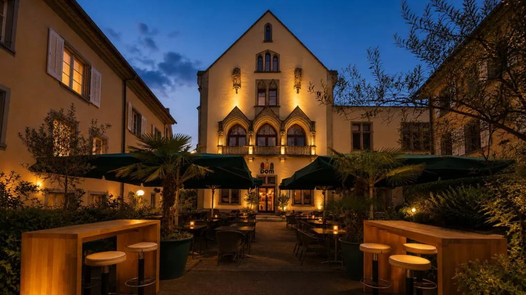 The Dom Konstanz – Gotische Fassade mit Terrasse, Palmen und Sonnenschirmen zur blauen Stunde in der Altstadt